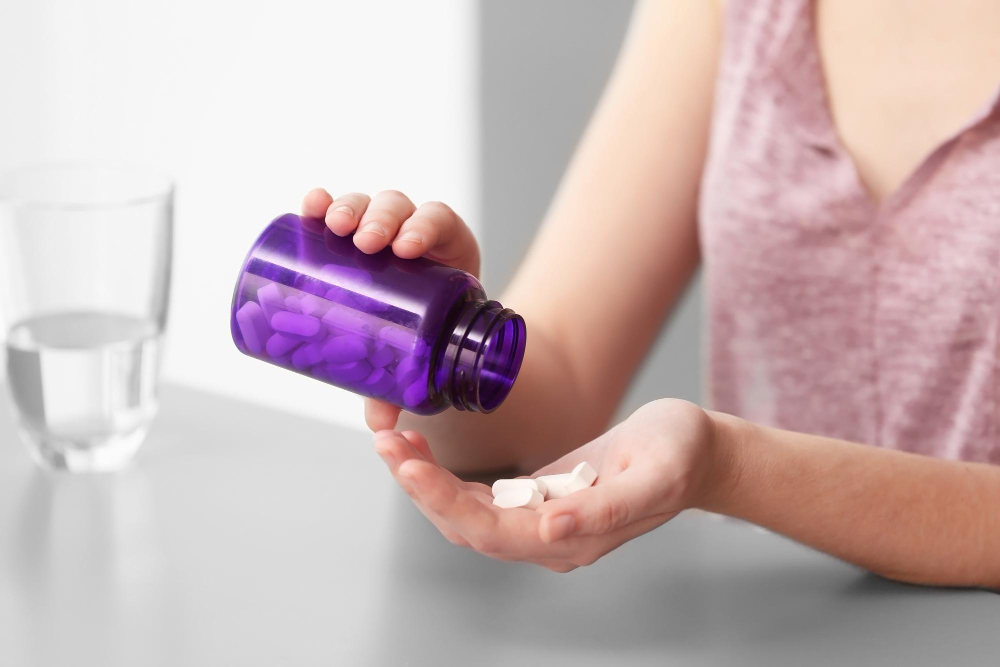 vrouw neemt supplementenpillen uit paars potje met glas water